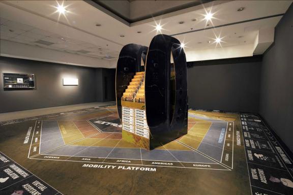 Simon Denny, (μπροστά) Caterpillar Biometric worker fatigue monitoring smartband Extractor pop display, 2019. (πίσω αριστερά) Caterpillar Inc. Biometric worker fatigue monitoring smartband promotion screen video token, 2019. (πίσω δεξιά) Speculative accountability trial courtroom sketch: Brisbane supreme court, Caterpillar Biometric worker fatigue monitoring wristband, 2020. Άποψη εγκατάστασης 7ης Μπιενάλε της Αθήνας 2021 ECLIPSE, φωτογραφία: Νύσος Βασιλόπουλος.