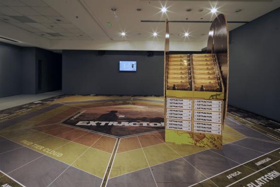 Simon Denny, (μπροστά) Caterpillar Biometric worker fatigue monitoring smartband Extractor pop display, 2019. (πίσω) Caterpillar Inc. Biometric worker fatigue monitoring smartband promotion screen video token, 2019. Άποψη εγκατάστασης 7ης Μπιενάλε της Αθήνας 2021 ECLIPSE, φωτογραφία: Νύσος Βασιλόπουλος.